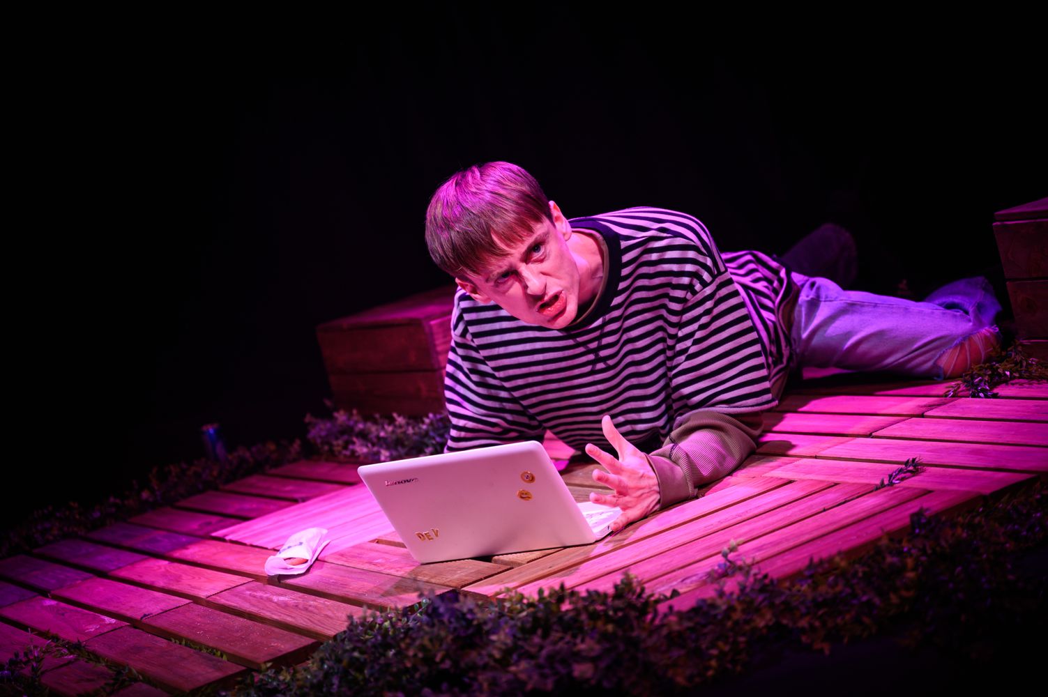 an actor lying on his front on stage with a laptop